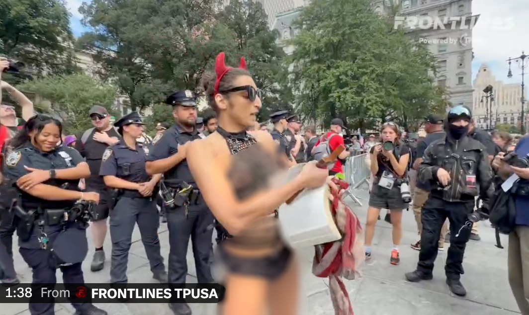 Un militant trans légèrement vêtu brandissant un crucifix arrache des pages de la Bible lors d'une manifestation contre le 11 septembre